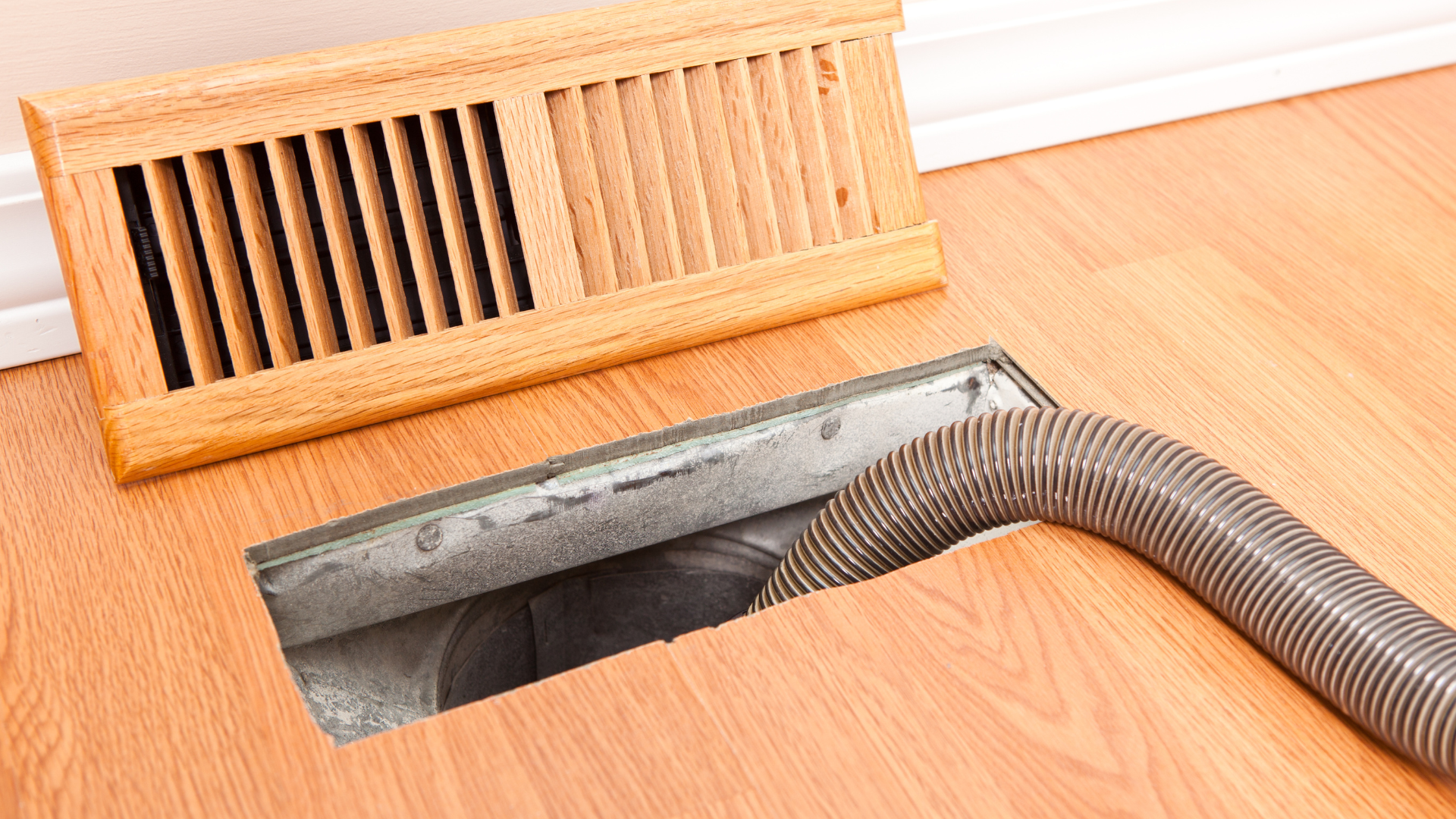 Technician kneeling beside an outdoor AC unit, using a wrench to repair refrigerant pipes.