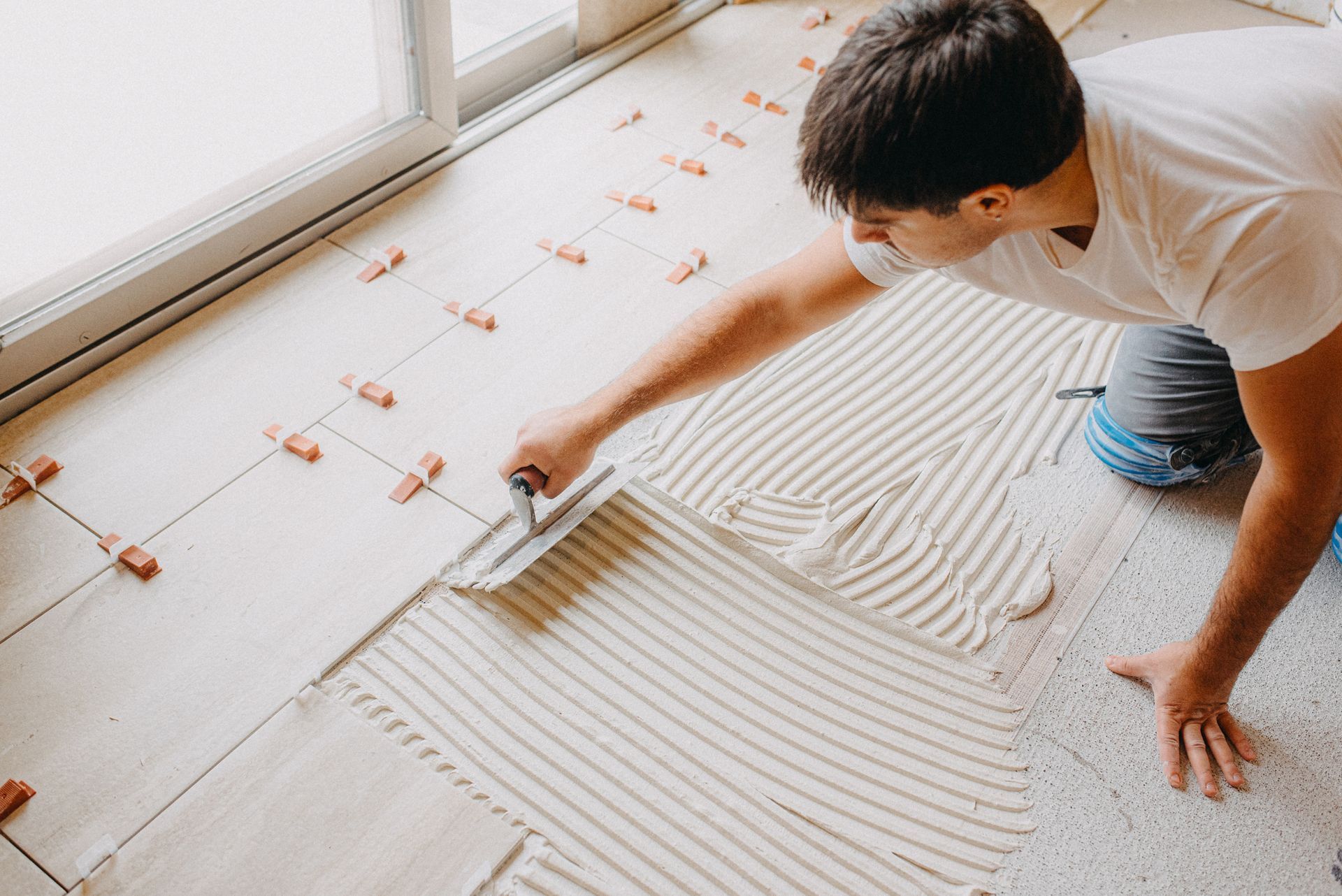Male construction worker spreads thin-set on the floor of a kitchen in state of remodeling.
