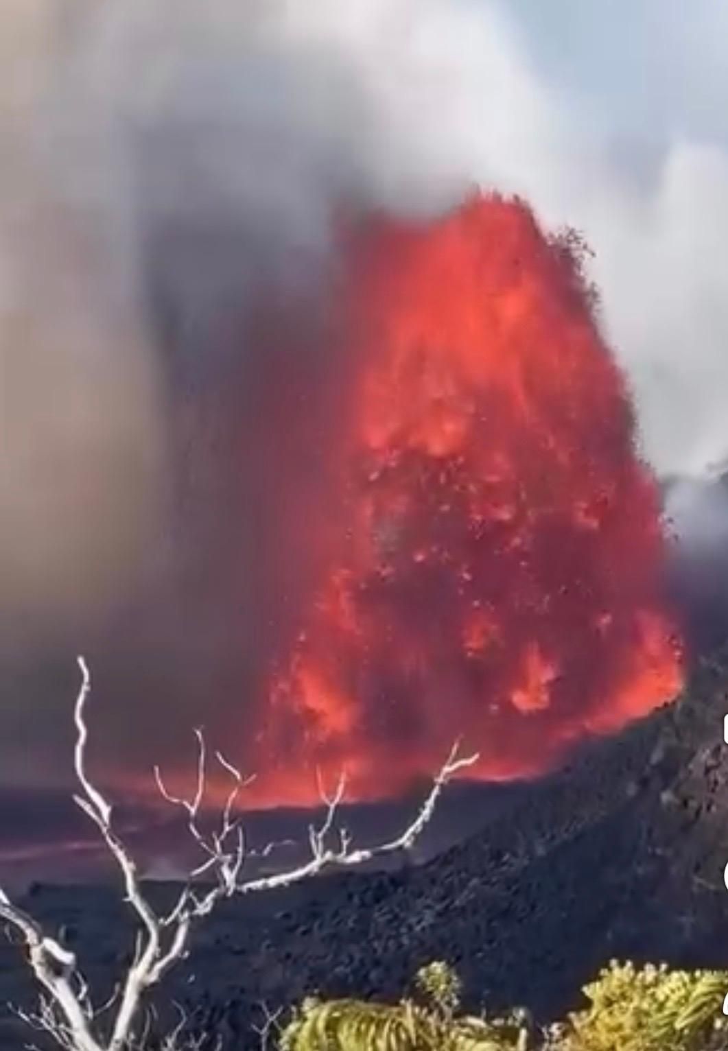 Volcanic eruption with bright orange lava and thick gray smoke rising over a barren hillside