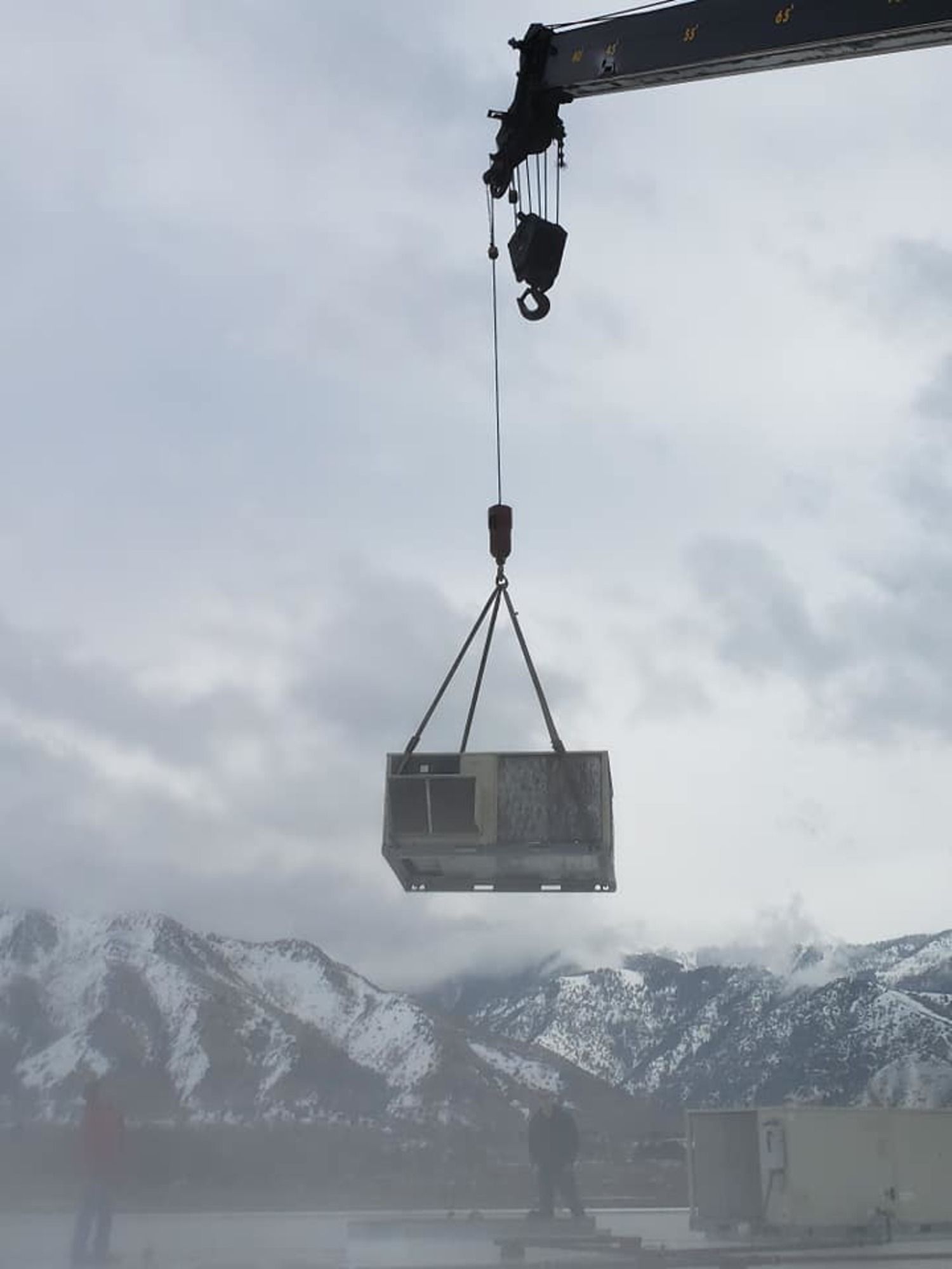 A large box is being lifted by a crane with mountains in the background
