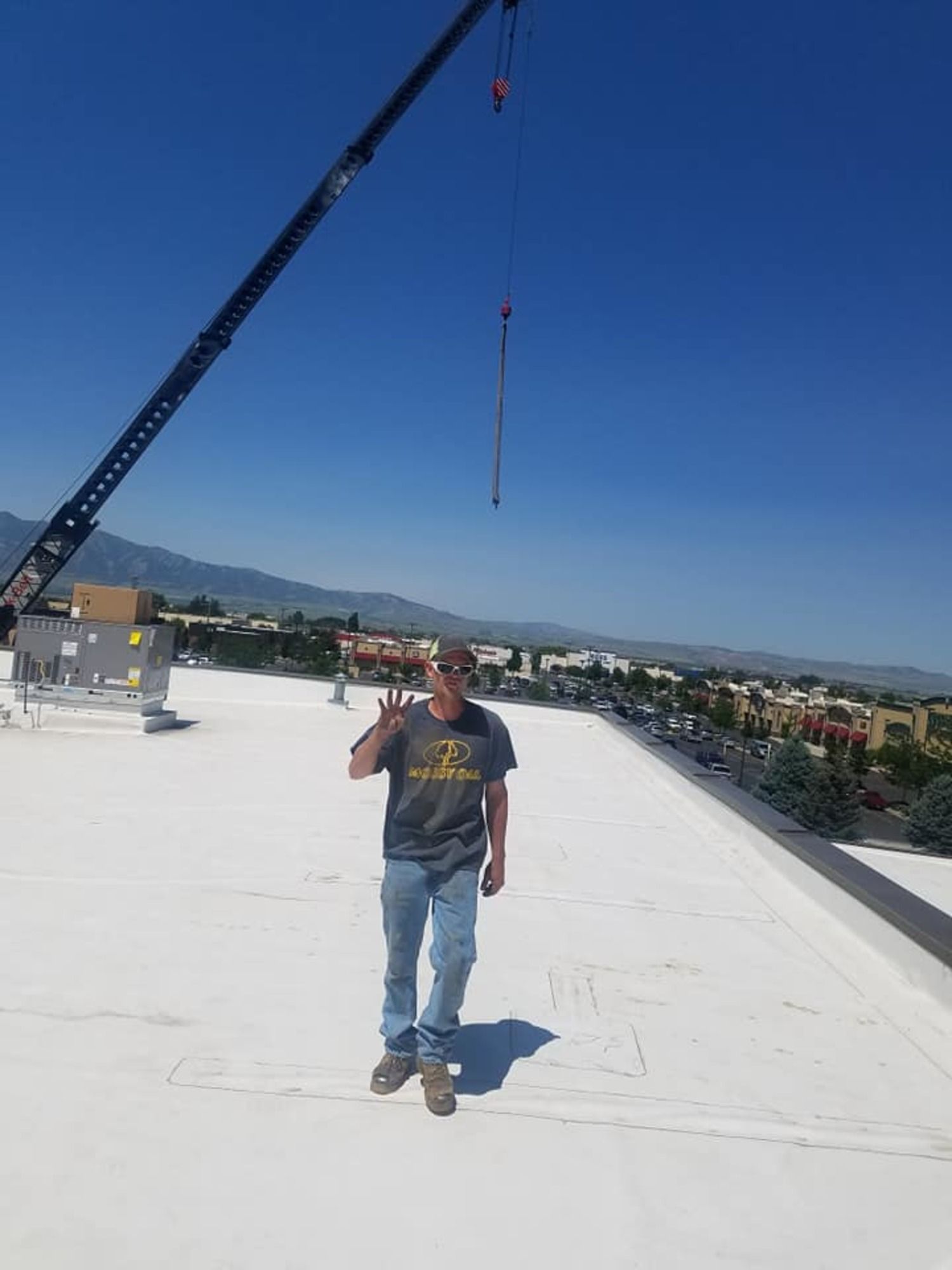 A man is standing on top of a white roof next to a crane.