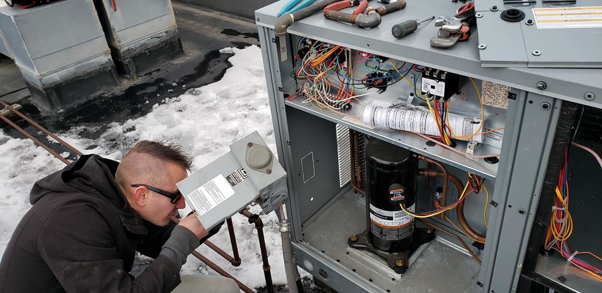 A man is working on an air conditioner outside in the snow.
