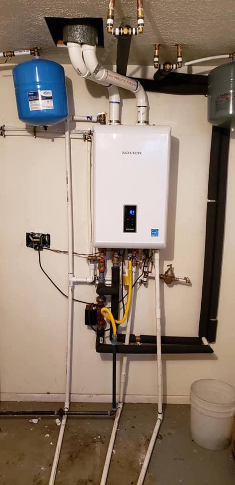 A white water heater is sitting in a basement next to a blue tank.