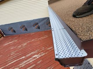 A person is standing on a wooden deck next to a metal gutter.