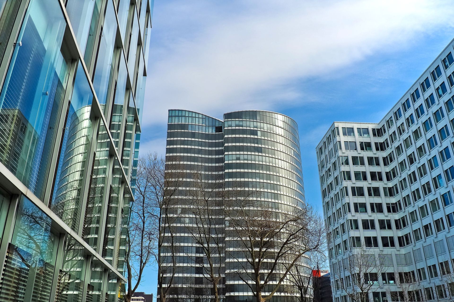 Ground view of three downtown, glass office buildings with a couple of small trees in front. 