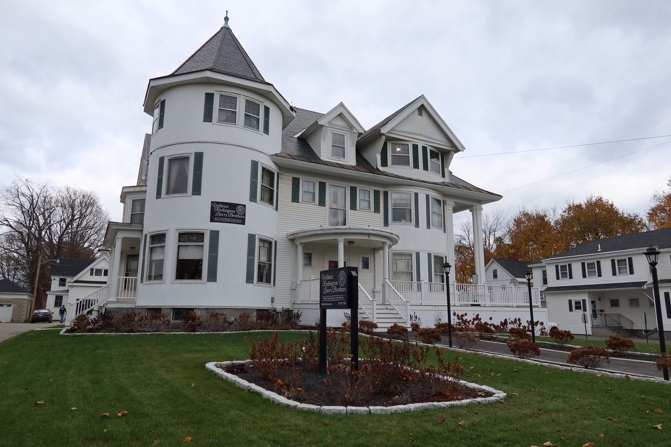 White Victorian building with a turret, green shutters, and a well-manicured lawn.