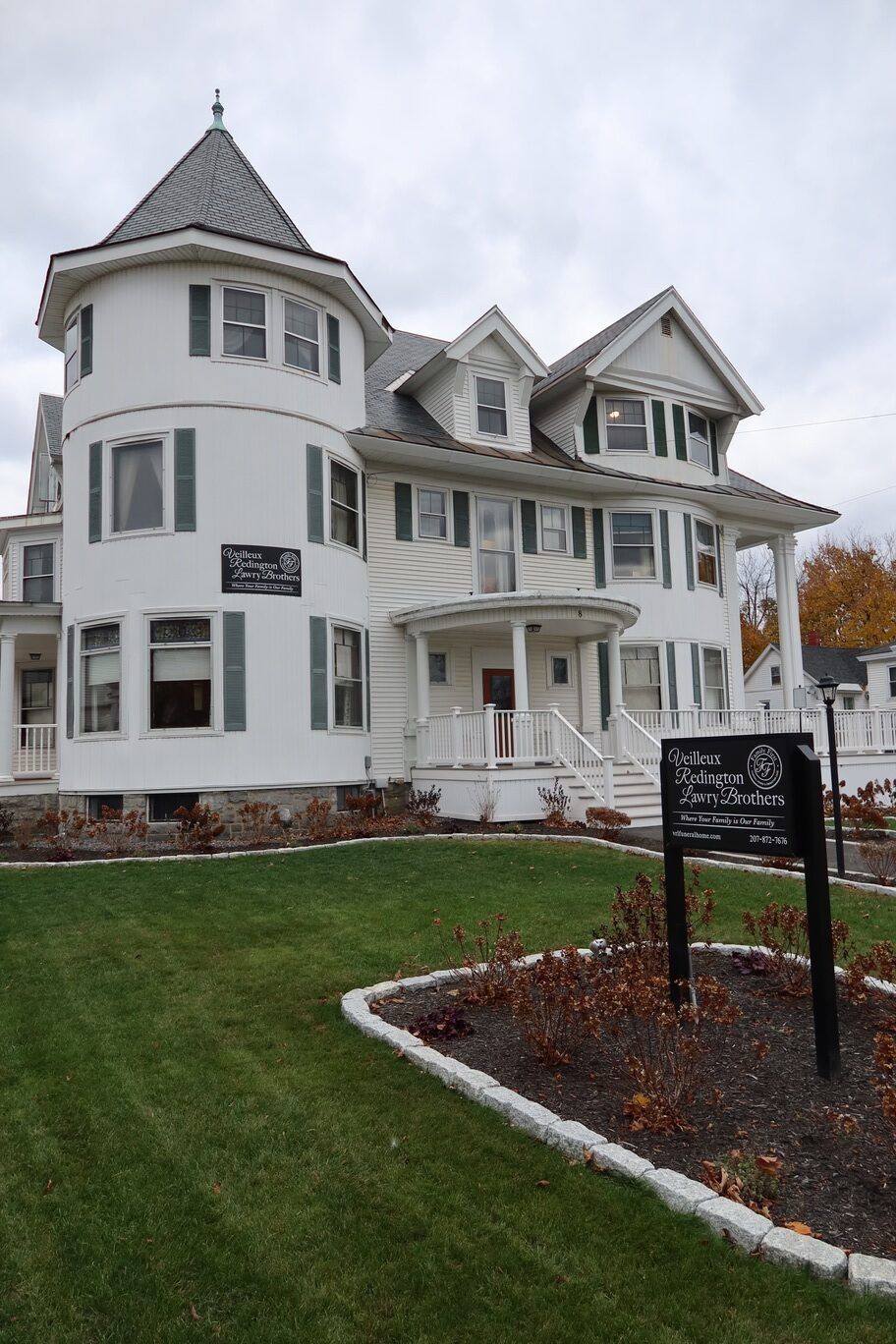 White Victorian house with a turret and green shutters, on a lawn with a sign.