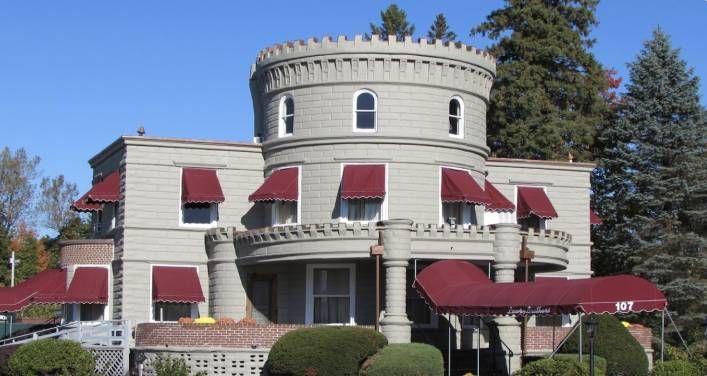 Castle-like building with a circular tower and red awnings, gray exterior. Sunny day.