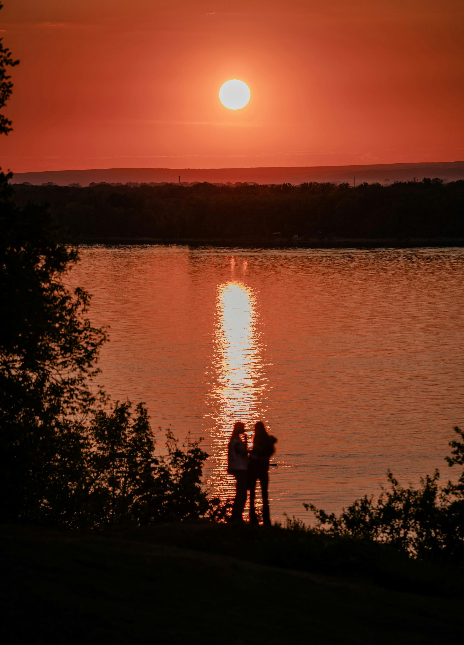 Silhouetted figures watching sunset over water, orange sky reflects on the lake.