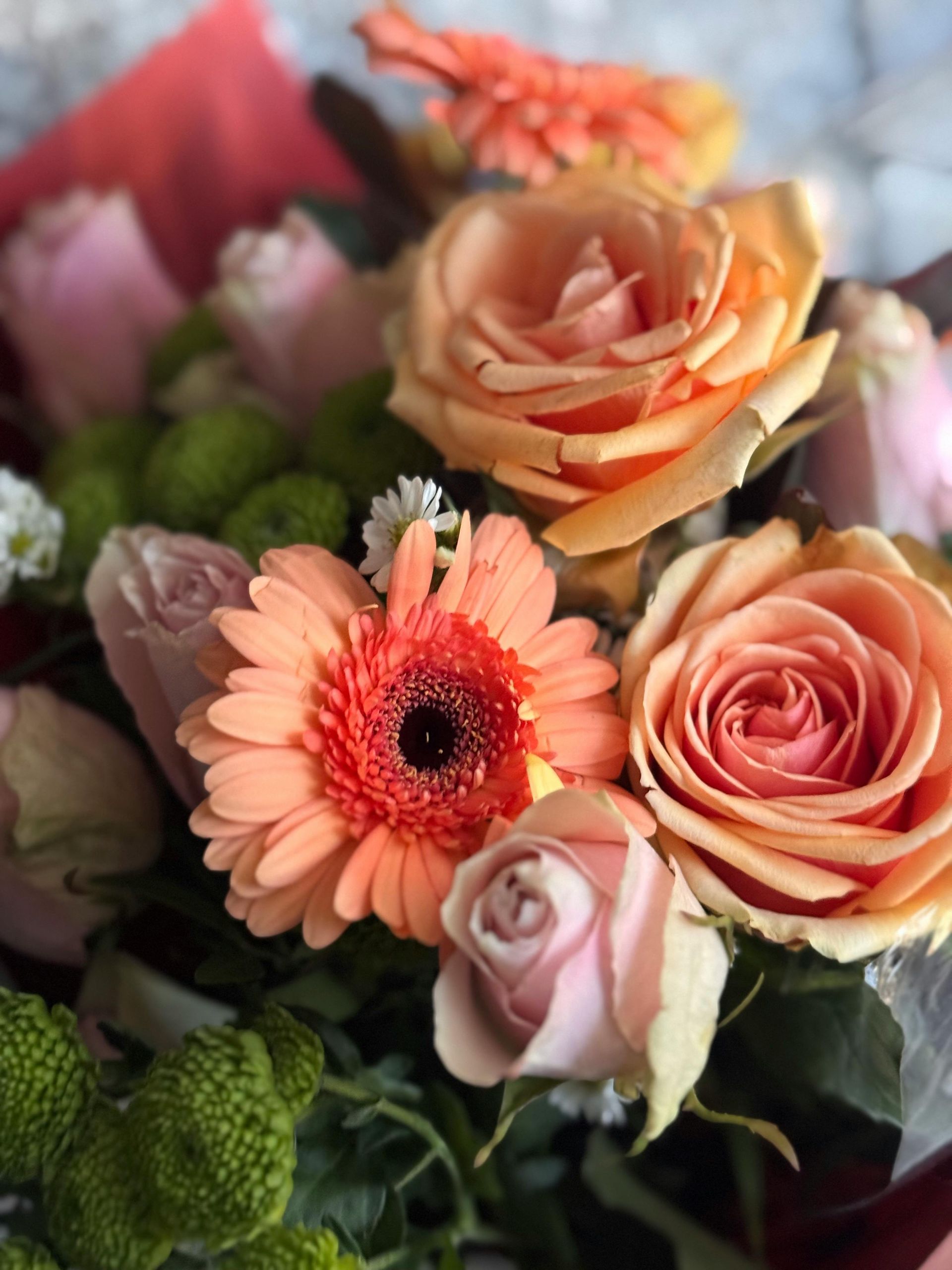 Bouquet of peach roses and orange gerbera daisies with greenery.