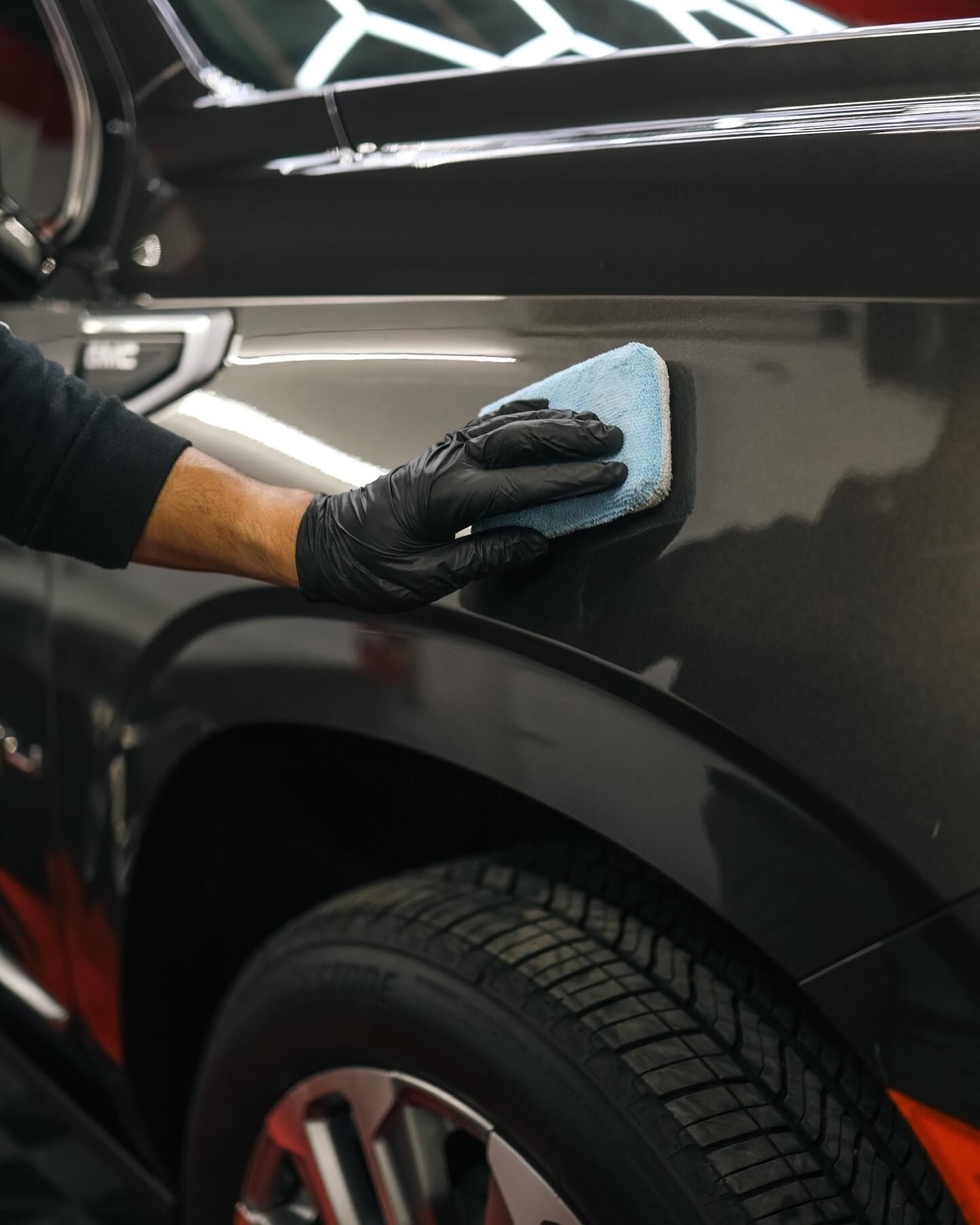 White Porsche SUV, close-up of front. Black headlight, grill, and trim. Red stripe detail. Interior shop setting.