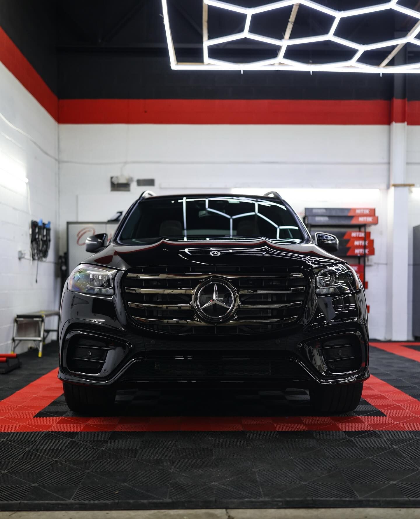 White Porsche SUV, close-up of front. Black headlight, grill, and trim. Red stripe detail. Interior shop setting.