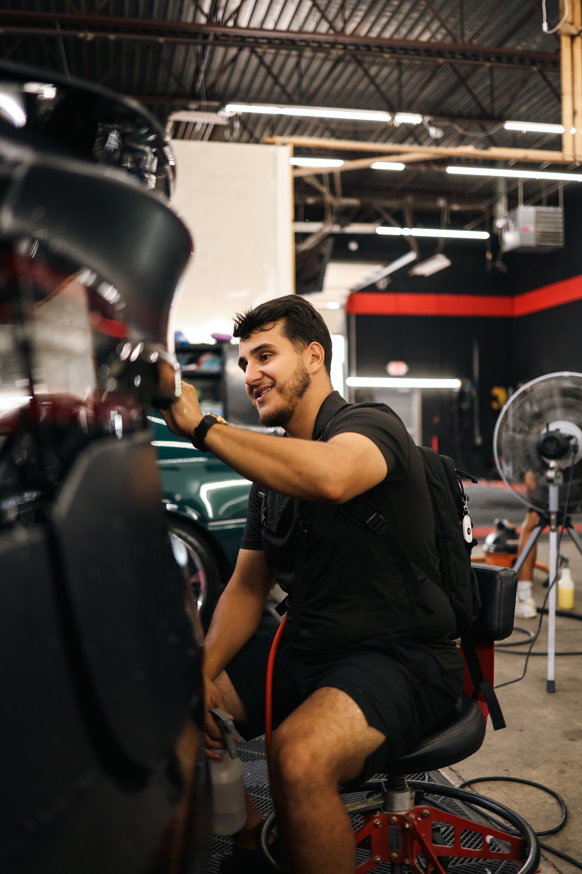 A man in a black hoodie is standing in front of a black car.