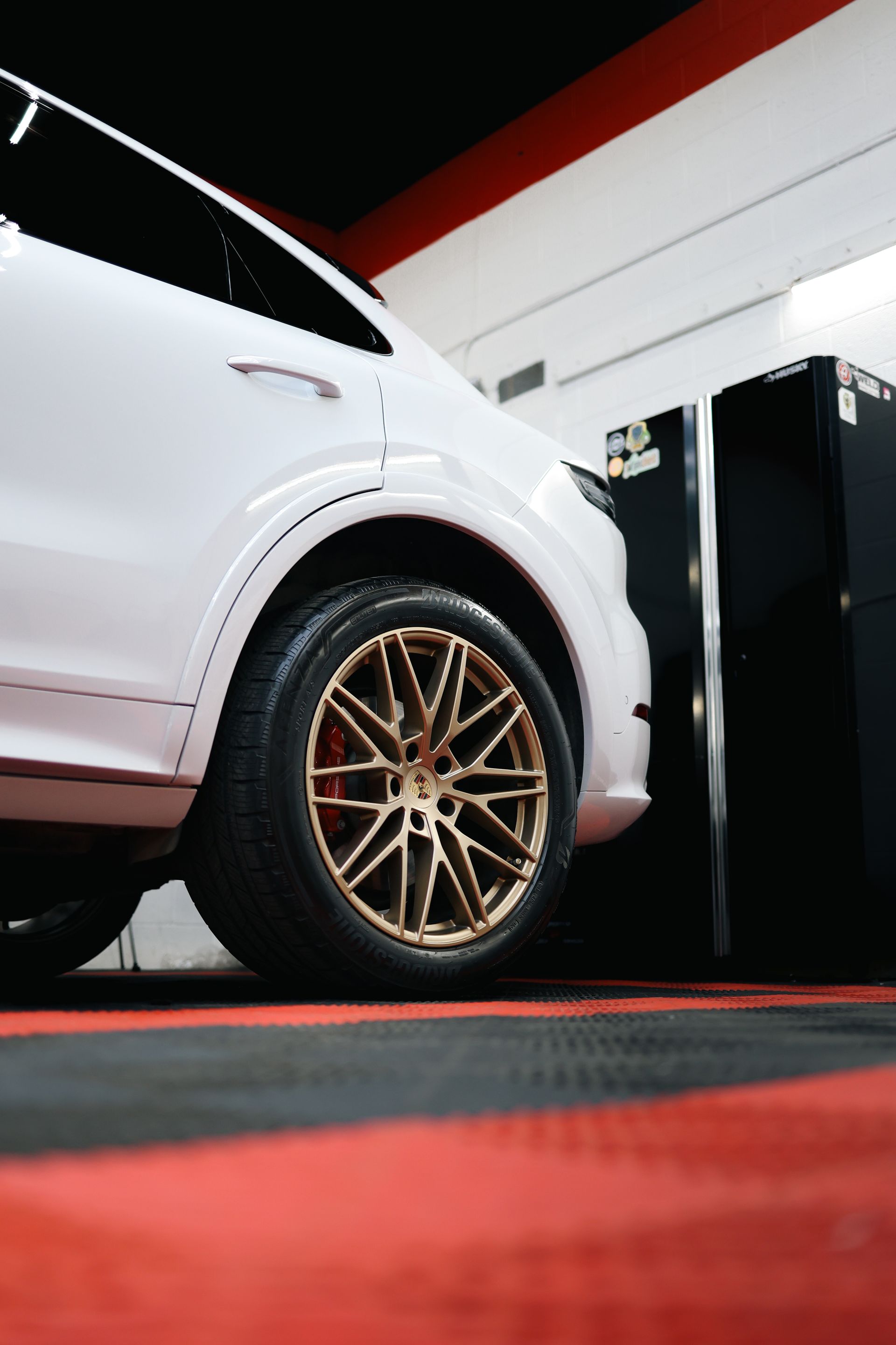 White car with gold rims on a red and black floor, against a white and black wall.