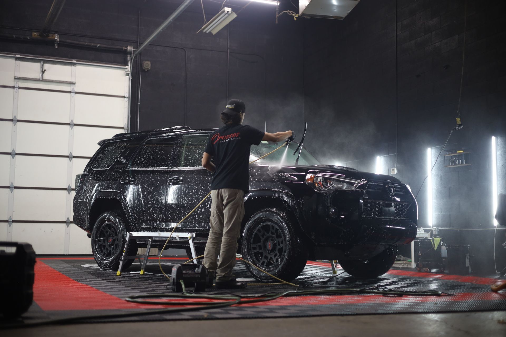 A man is washing a black suv in a garage.