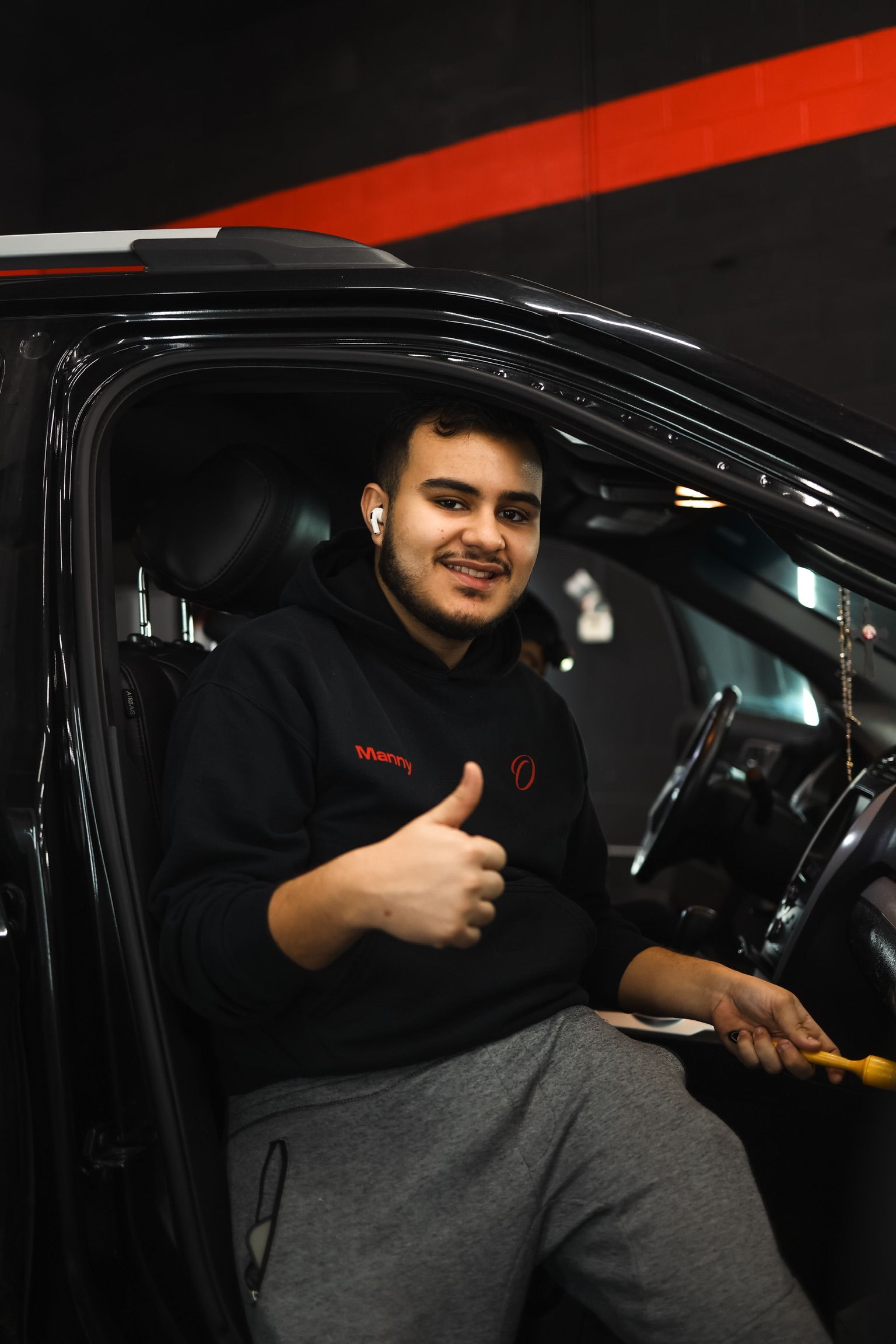 A young man standing in front of a red car with his arms crossed