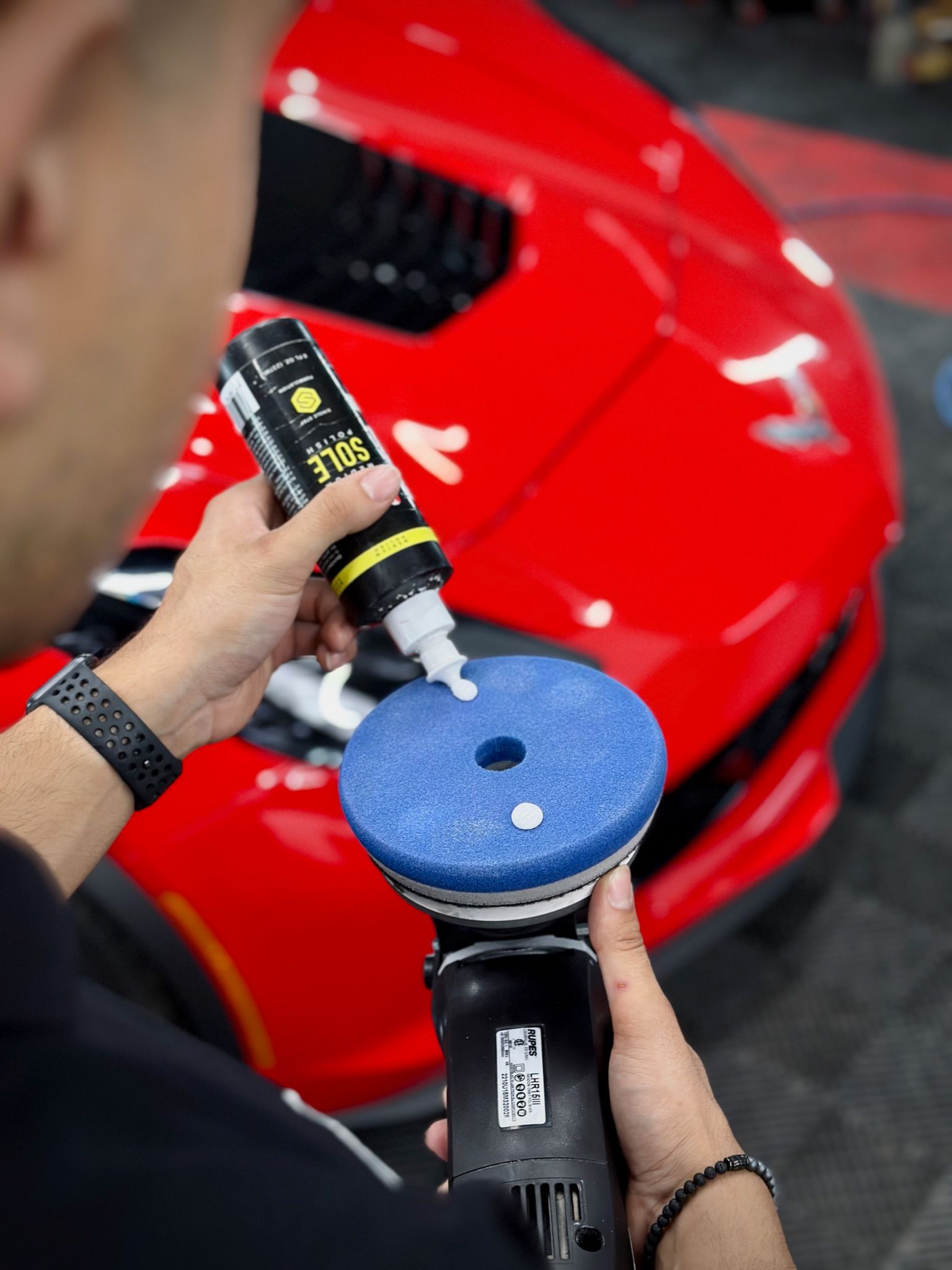 Person applying polishing compound to a blue buffing pad on a red car.