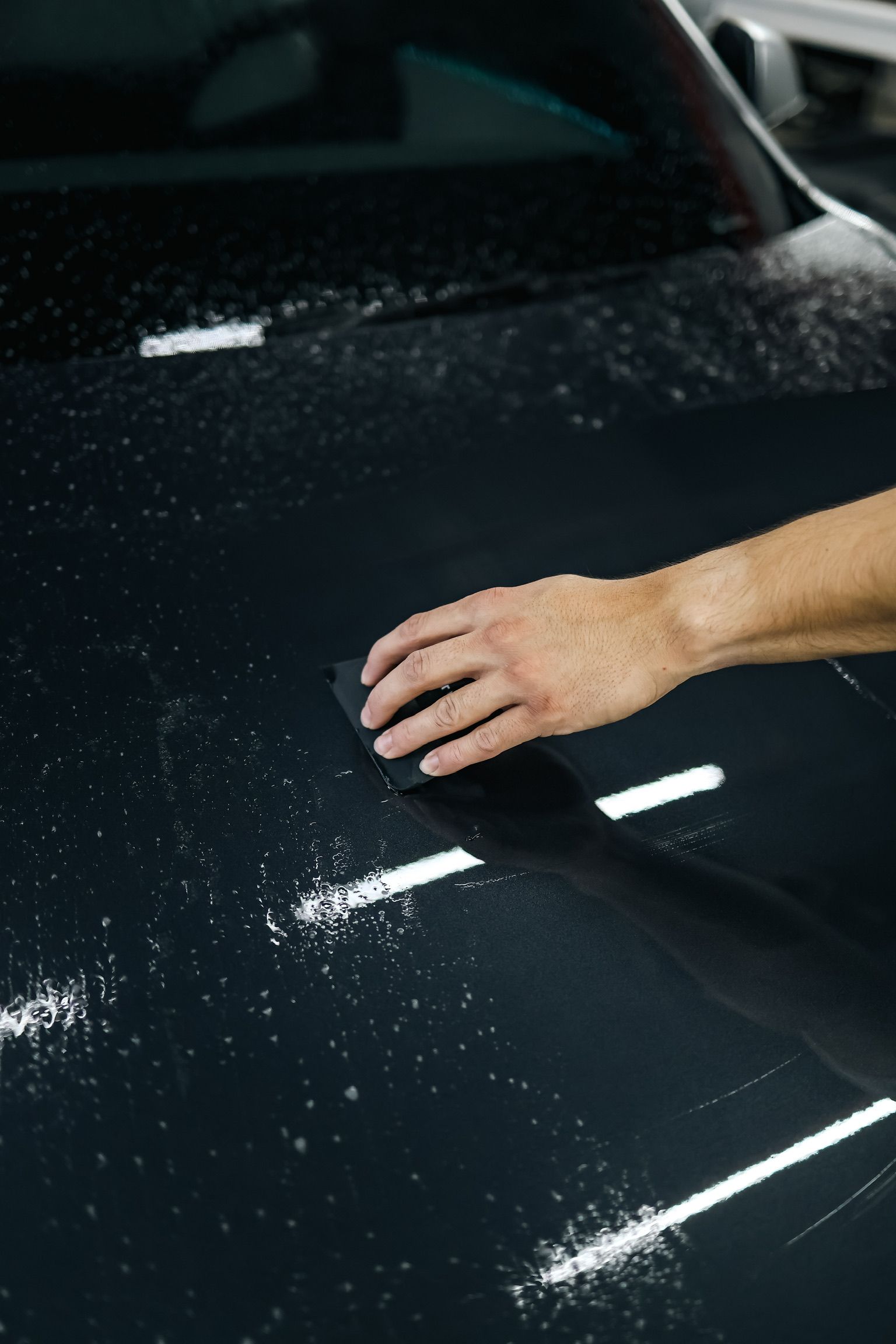 A person is cleaning the hood of a car with a sponge.