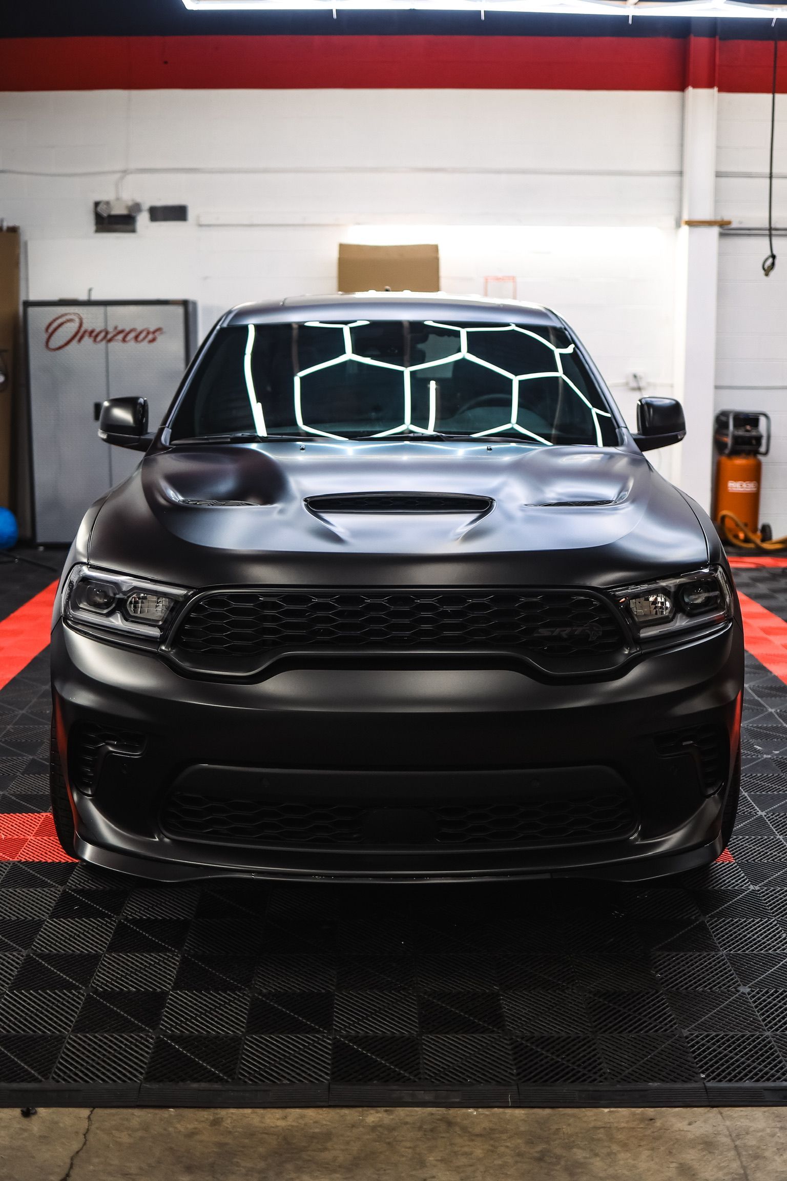 A black car is parked on a checkered floor in a garage.