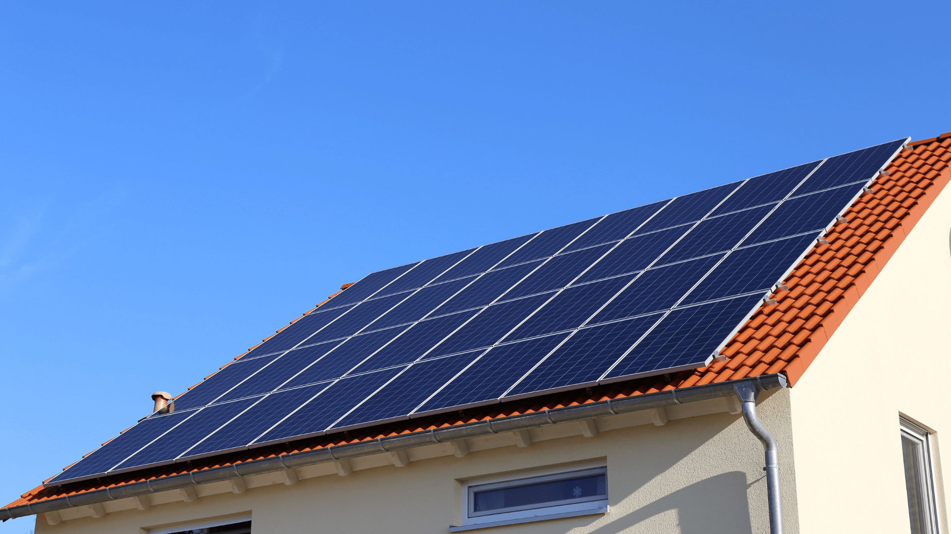 Solar panels on a red-tiled roof of a house, against a clear blue sky — OzEnergi in Caloundra West, QLD