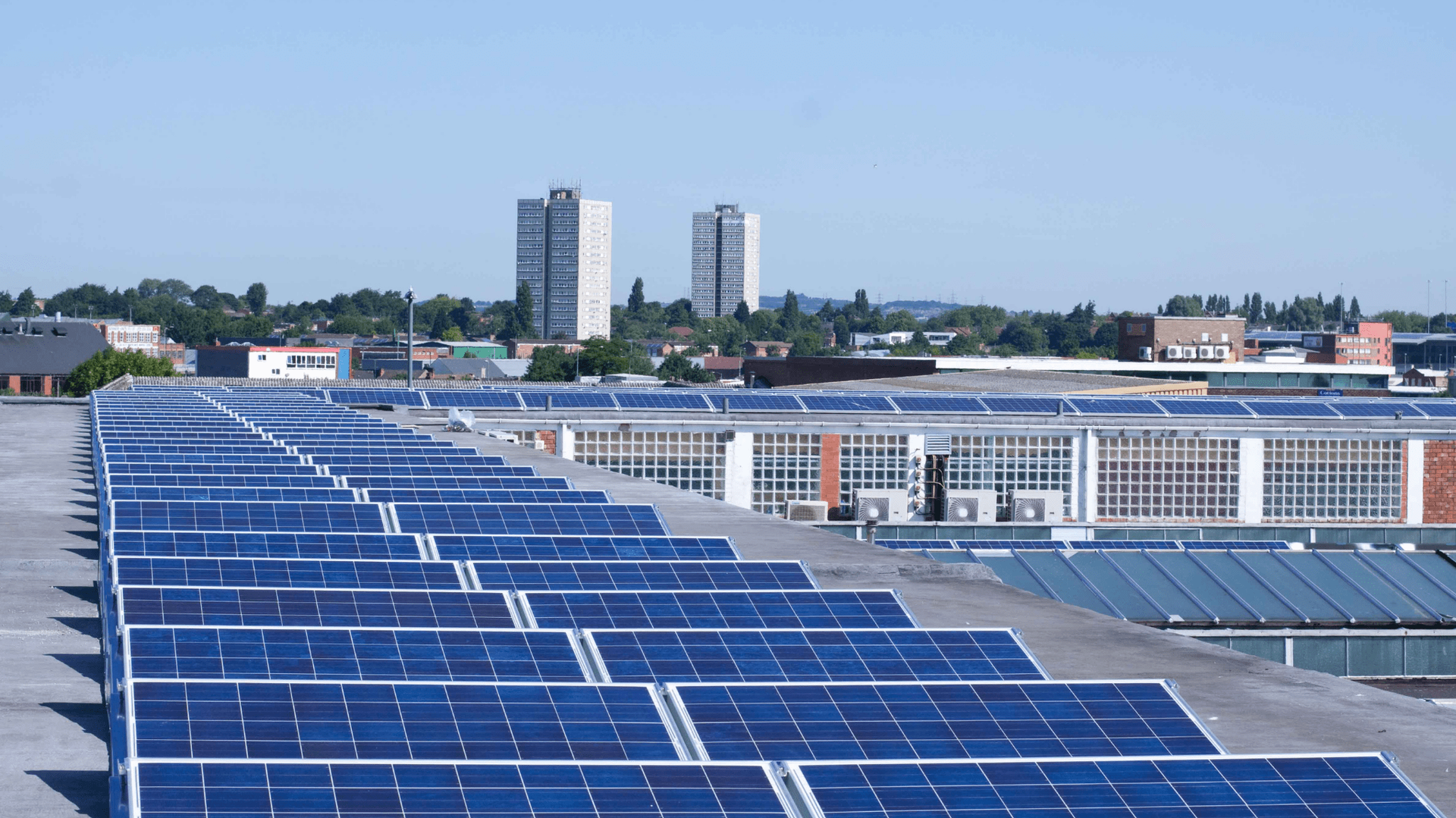 Solar panels on a building rooftop, with city skyline and blue sky in the background 