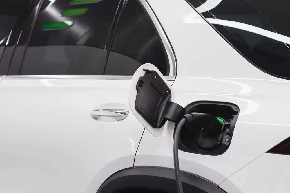 White electric car charging, charging port open, black charging cable plugged in.  — OzEnergi in Coomera, QLD