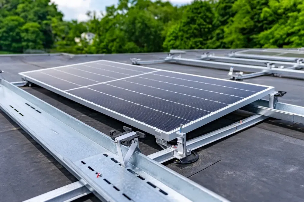 Solar panel mounted on a flat black roof, surrounded by metal racking, with trees in the background. — OzEnergi in Southport, QLD