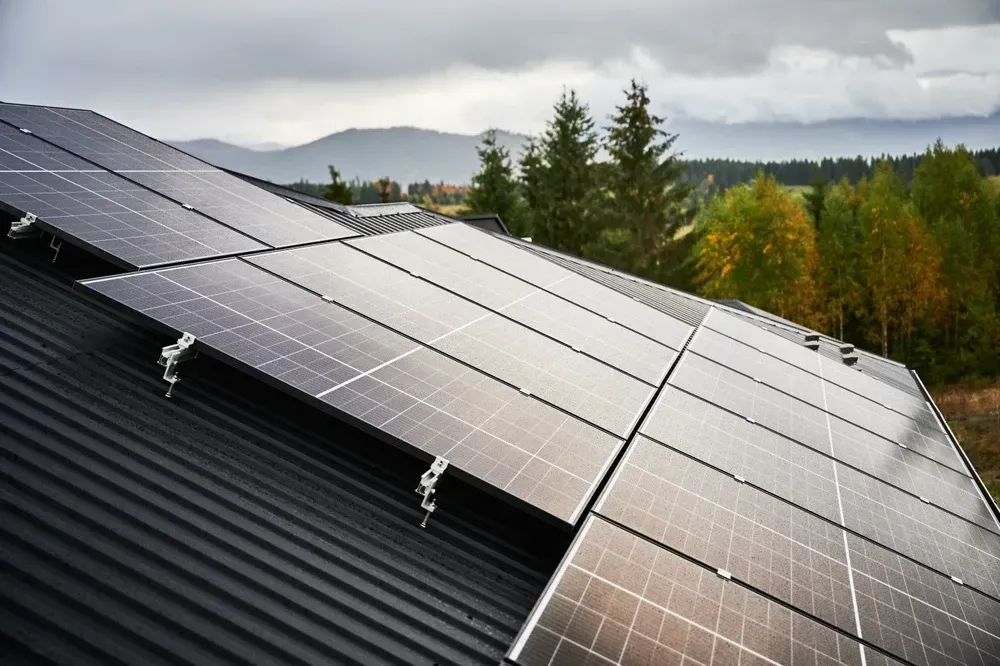 Solar panels on a sloped roof with a mountain and trees in the background. — OzEnergi in Coomera, QLD