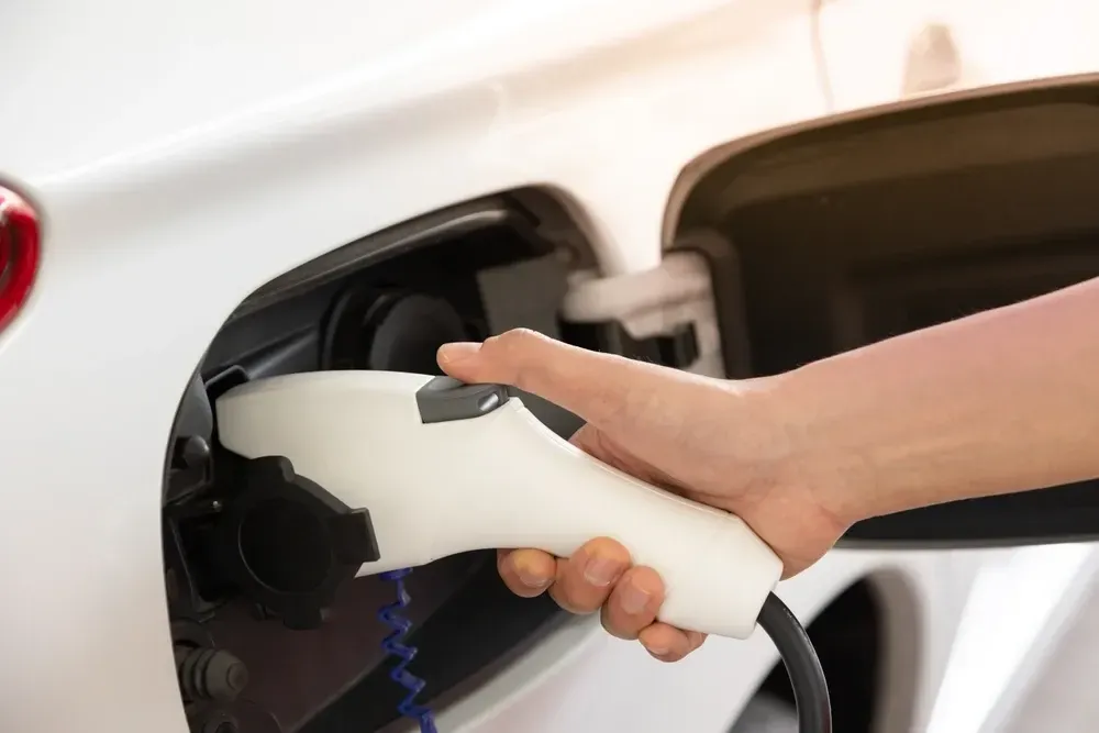 Hand plugging a white charging cable into the charging port of a white electric car. — OzEnergi in Mermaid Beach, QLD