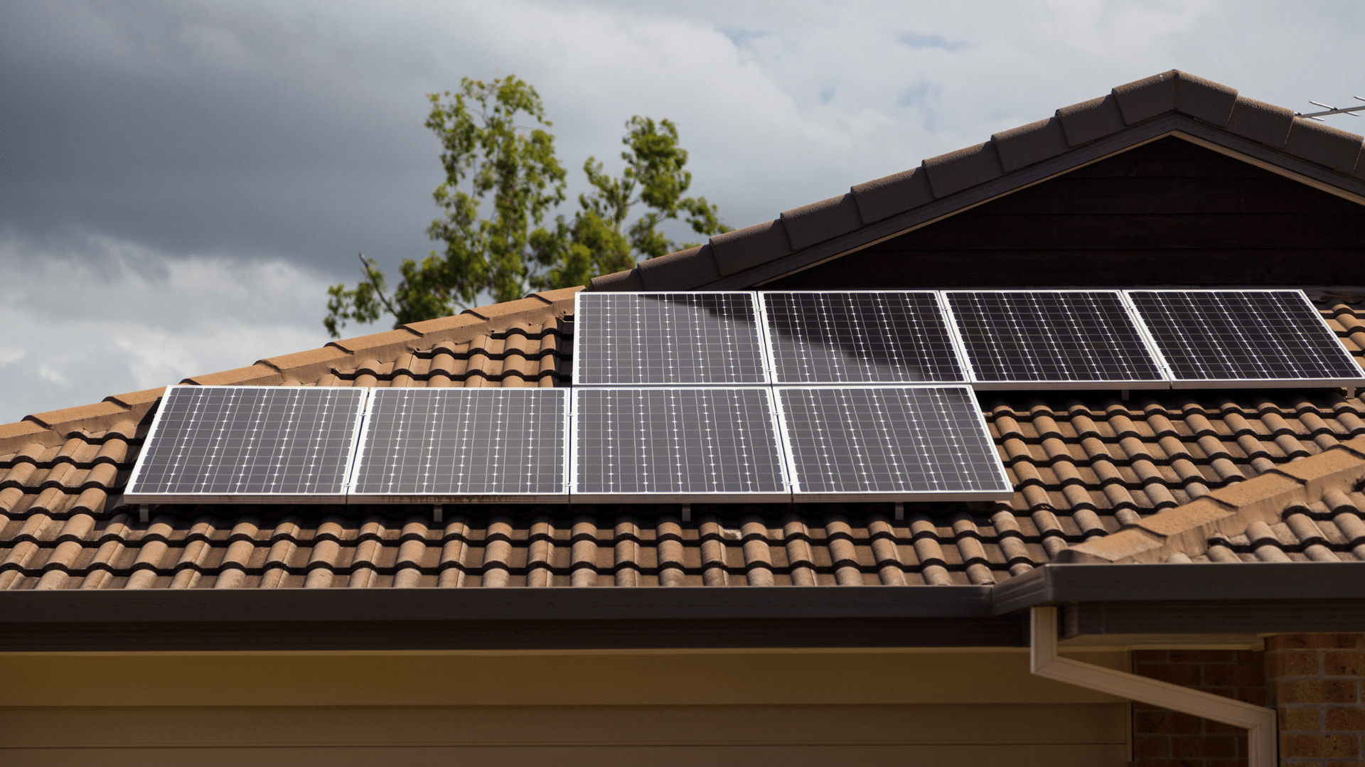 Solar panels on a brown tiled roof under a cloudy sky — OzEnergi in Caloundra West, QLD