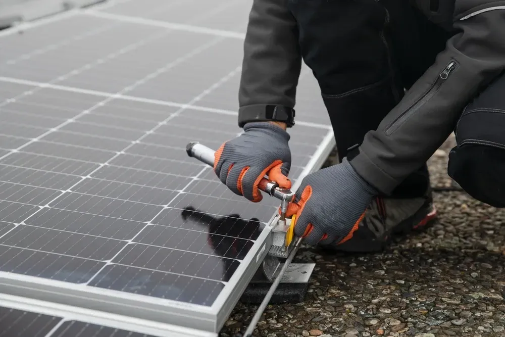 Person installing solar panel on a rooftop, using a wrench. Wearing gloves and dark work clothes.  — OzEnergi in Burleigh Heads, QLD