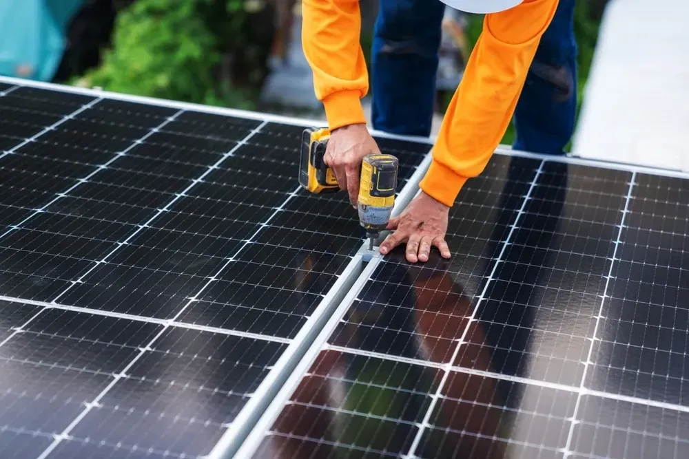 Person in orange shirt installing solar panels with a drill. — OzEnergi in Coomera, QLD