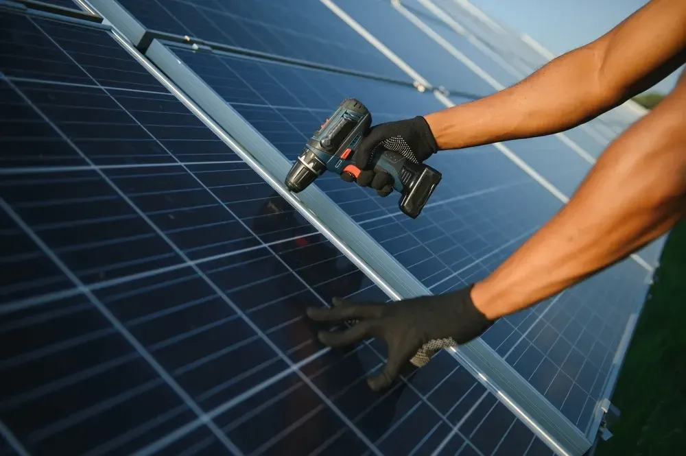Person in gloves using a power drill on a solar panel. — OzEnergi in Southport, QLD