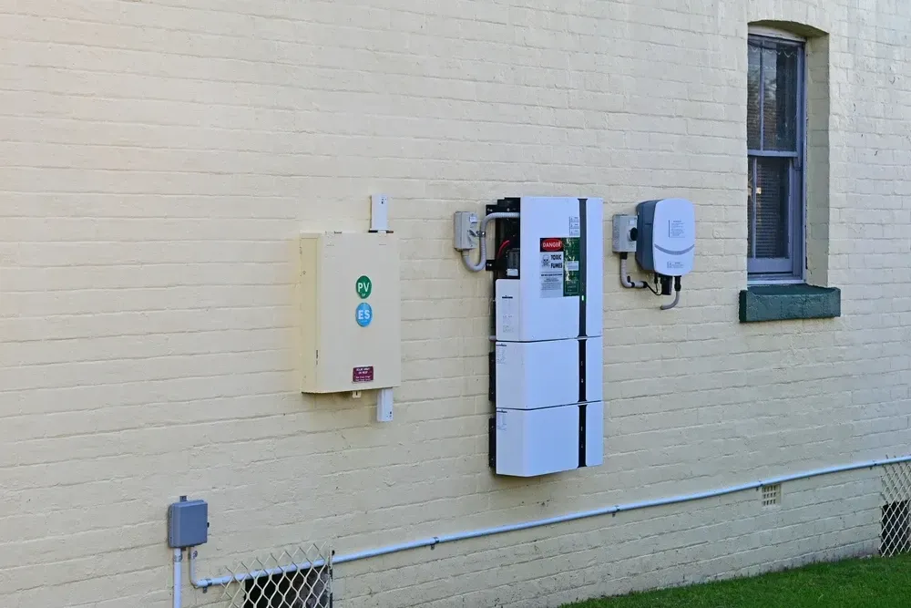 Solar power components mounted on a cream-colored exterior wall near a window. — OzEnergi in Coomera, QLD