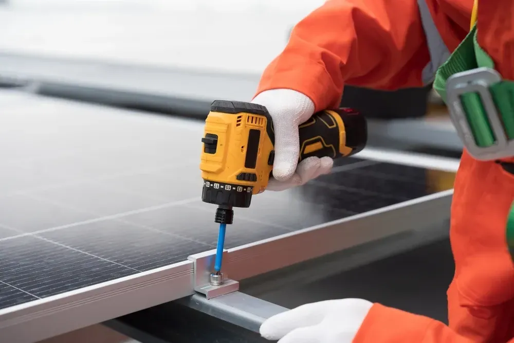 Worker in orange coveralls installing a solar panel, using a yellow and black power drill. — OzEnergi in Yatala, QLD