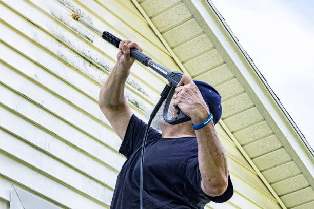 A man is using a high pressure washer to clean the side of a house.