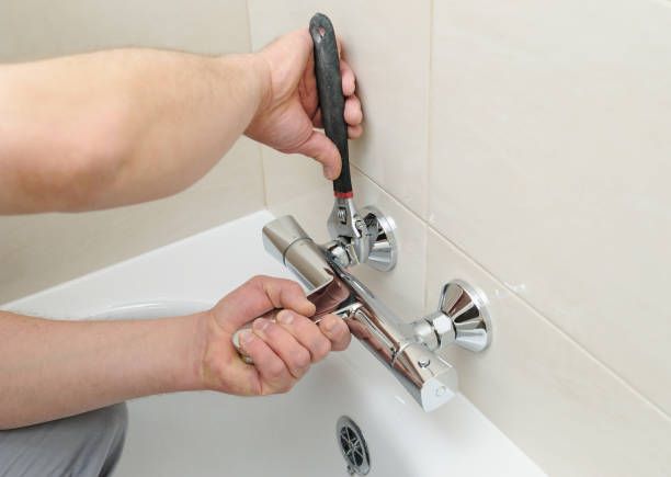 A man is fixing a bathtub faucet with a wrench.