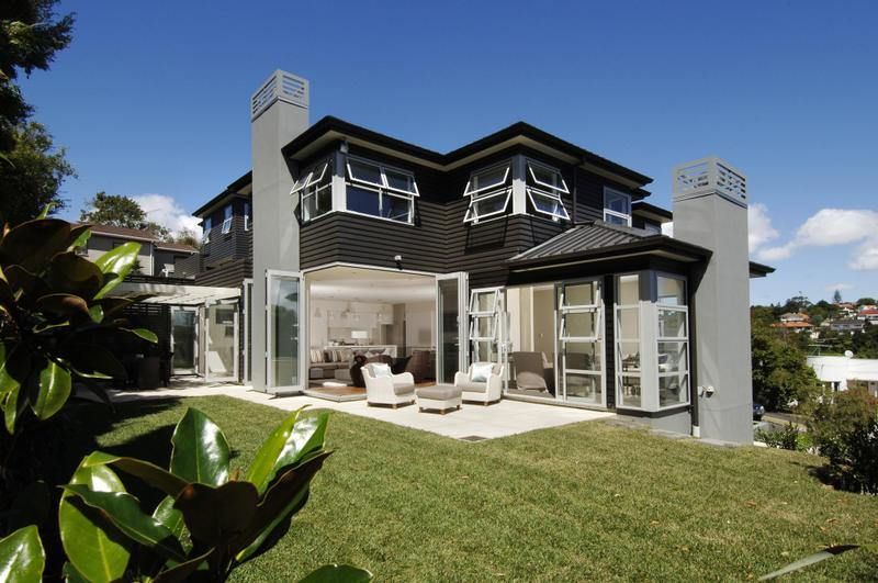 Two-story house with black roof, gray exterior, and open glass doors leading to a patio with white furniture.