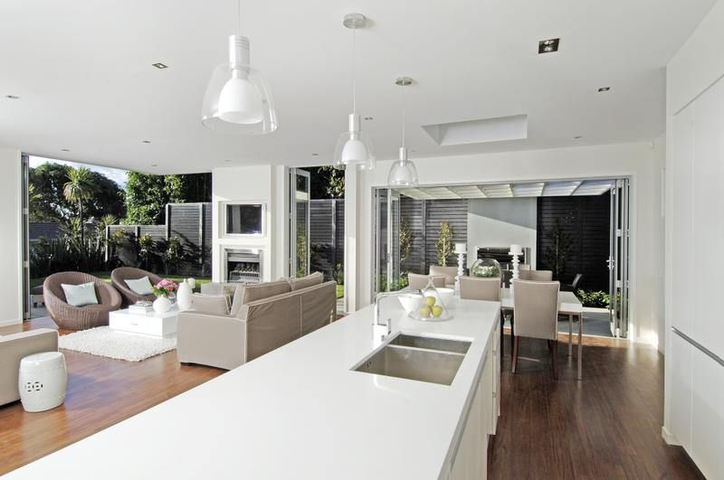 Modern open-plan kitchen and living room with outdoor access. White countertops, dark wood floors, and neutral furnishings.