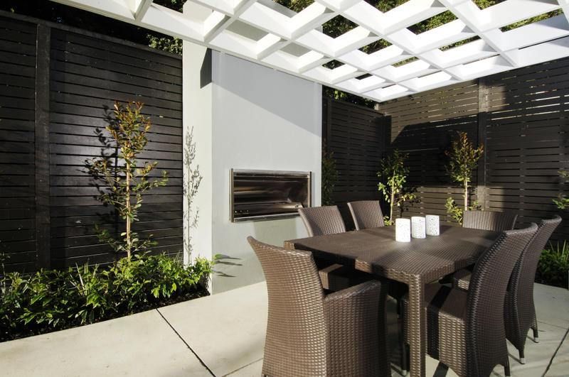 Outdoor dining area with a grill, table, chairs, and overhead lattice structure.
