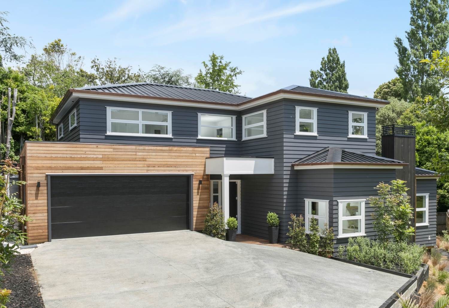 Two-story house with dark gray siding, wooden garage door, and light brown wood accents.