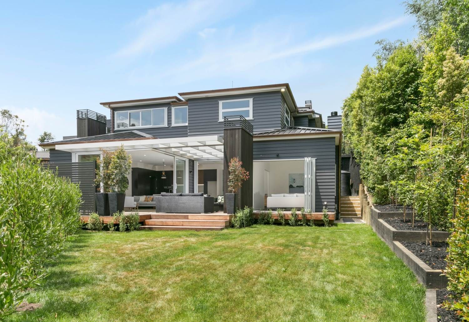 Two-story house with black exterior, wooden deck, and green lawn; climbing plants on the right.