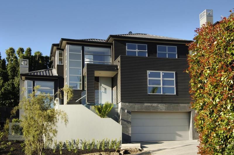 Modern two-story house with dark siding, multiple windows, and a gray garage door.