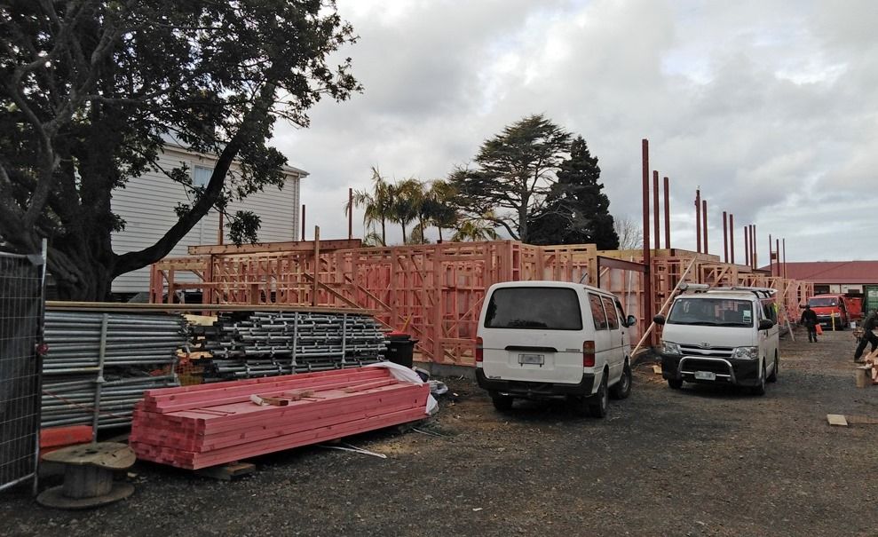 Construction site with exposed wooden framing and several vehicles. Gray sky.