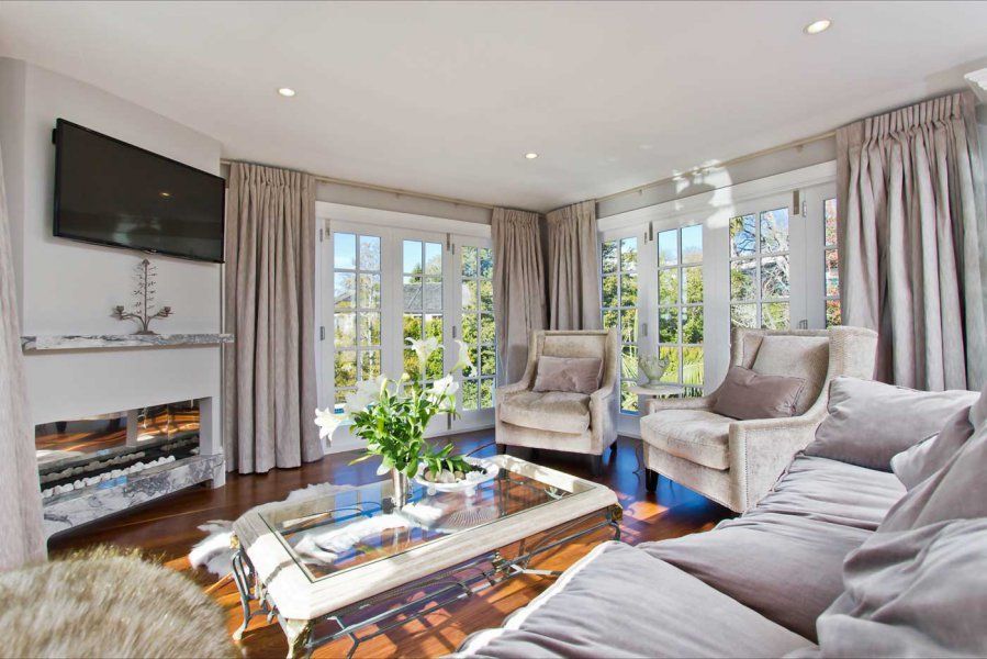 Living room with gray sofa, armchairs, curtains, and glass-top coffee table in front of French doors.