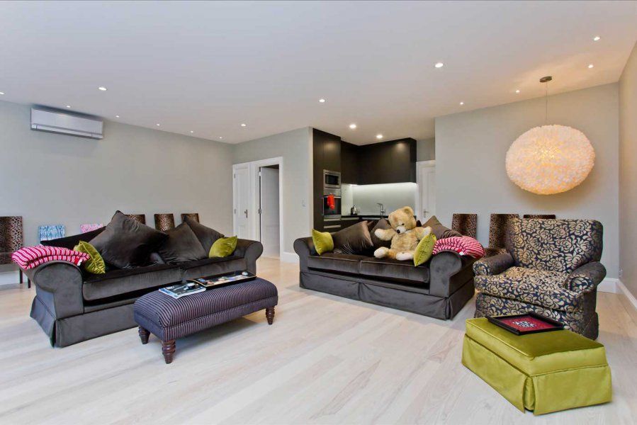 Living room with gray sofas, a patterned armchair, and a small kitchen visible in the background.