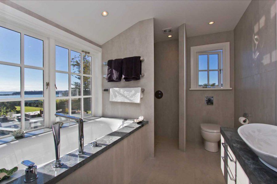 Bathroom with tub under large windows, toilet, and sink. Neutral colors, scenic view outside.