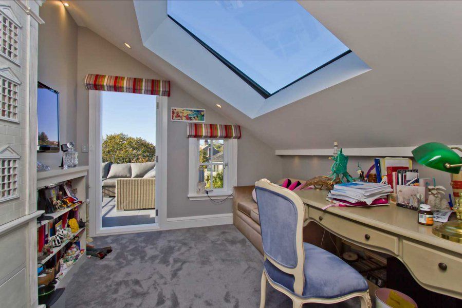 Attic room with desk, skylight, and open doorway to patio. Gray carpet, gray walls, and colorful striped accents.