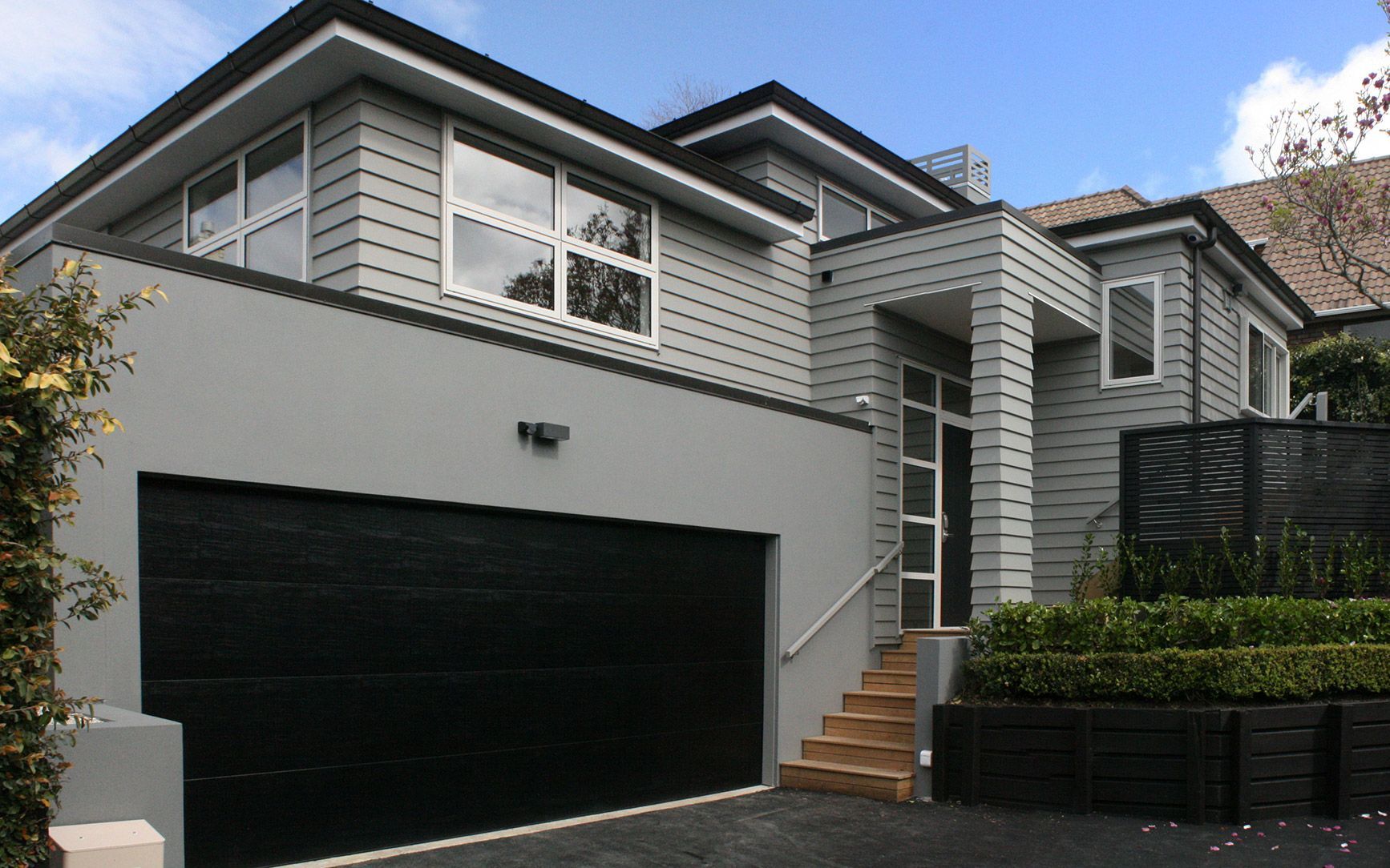 Gray modern house with black garage door, stairs, and dark trim.