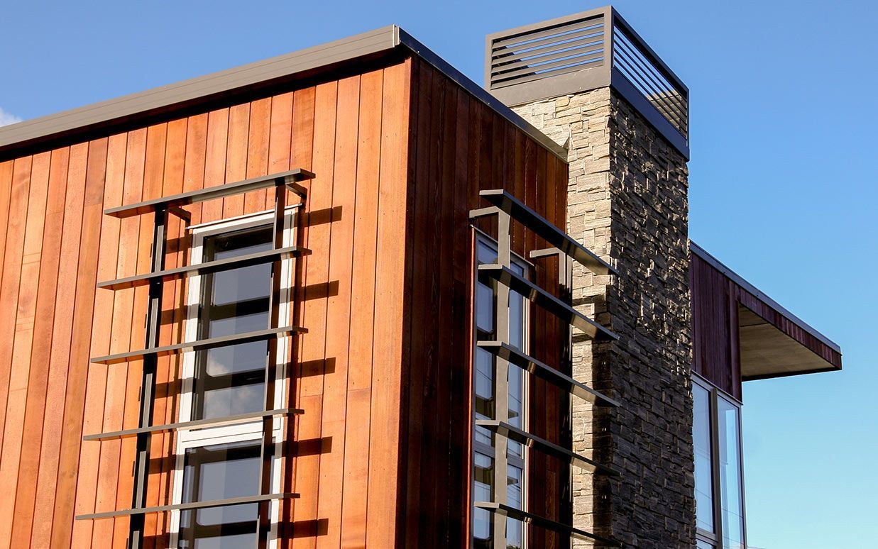 Modern building with textured wood siding, stone chimney, and metal window accents against a blue sky.